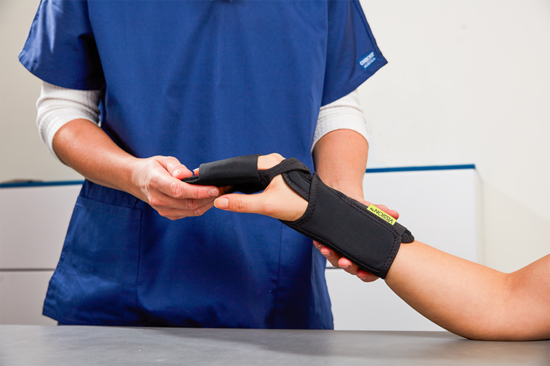 Beskuren bild på en person i blå vårdklädsel som provar ut fingerortosen VISSION Finger Splint POSI på en person vars hand och underarm vi ser. VISSION Finger Splint POSI är ett ortopedtekniskt hjälpmedel från Camp Scandinavia.